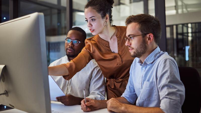 small team of three people gathered around a computer monitor collaborating on a project
