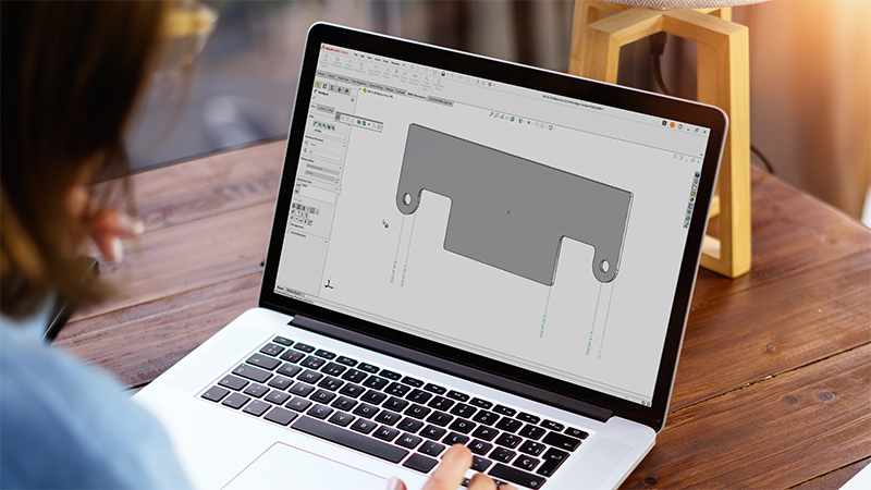 Designer working on a laptop with a screen showing a 3D model of a part