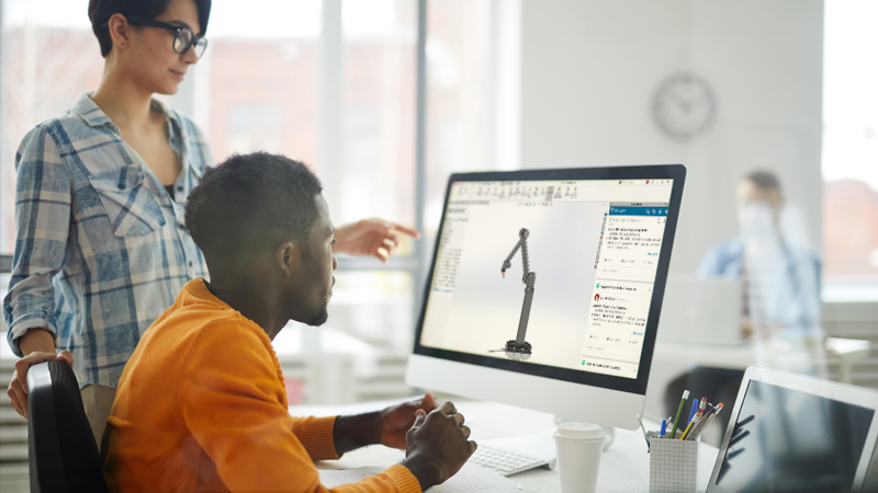 People working on SOLIDWORKS 3D model on a monitor in an office setting