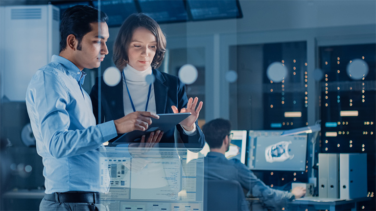 Two colleagues in discussion over laptop. Servers in the background.