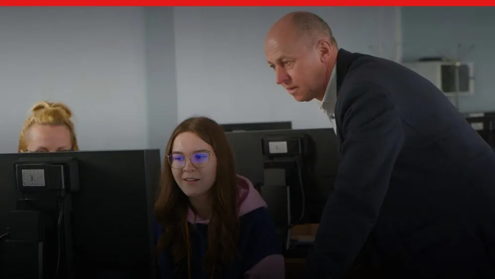 Ausbilder schaut zwei Studierenden über die Schulter und auf Computerbildschirme